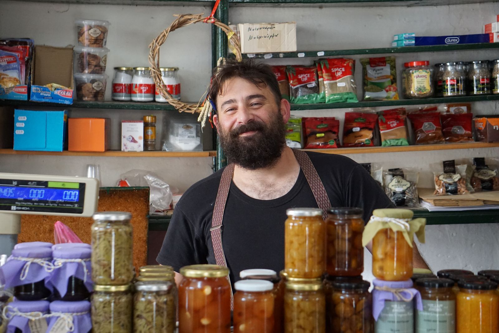 A shopkeeper smiling behind a counter of jars of preserves he made.