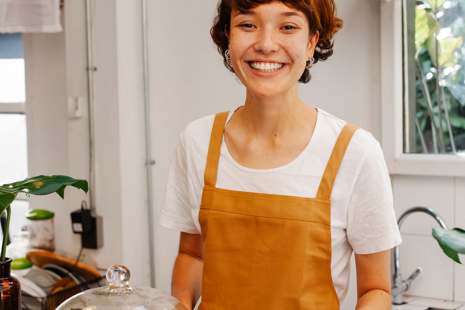 A baker in an ochre apron smiling behind her counter.