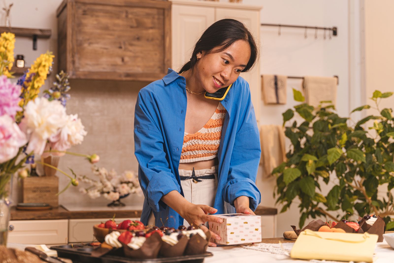 A woman arranging flowers and produce at a wooden work table.
