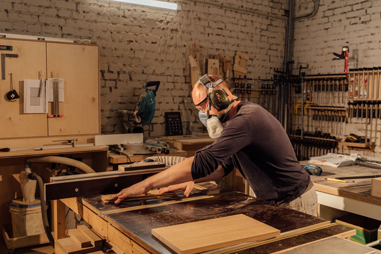 A joiner planing a board in a brick-walled workshop.